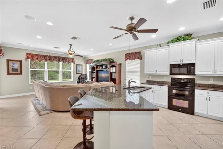 Kitchen featuring black appliances, a kitchen breakfast bar, open floor plan, white cabinetry, and light tile patterned flooring