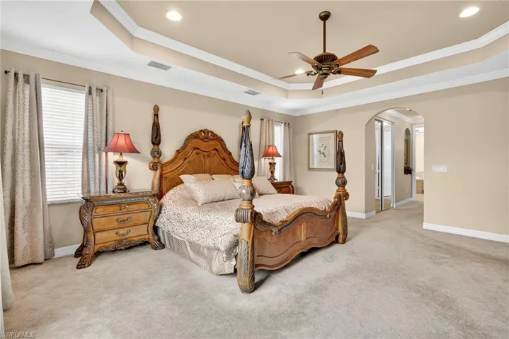 Bedroom with a tray ceiling, crown molding, light carpet, and multiple windows