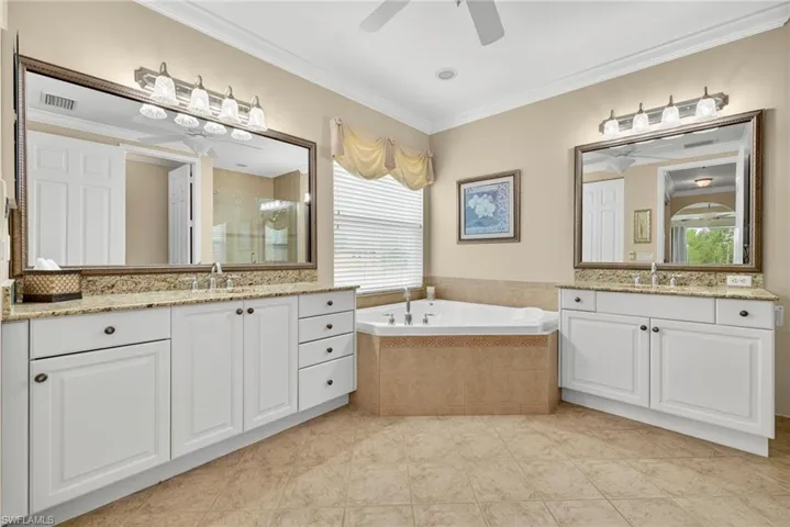 Full bath featuring ornamental molding, a stall shower, two vanities, a bath, and light tile patterned floors