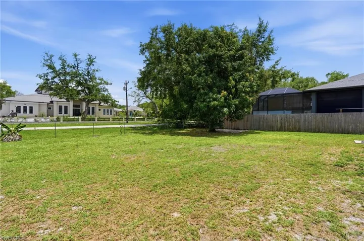 Expansive grass lot featuring a mature tree, bordered by a wood privacy fence
