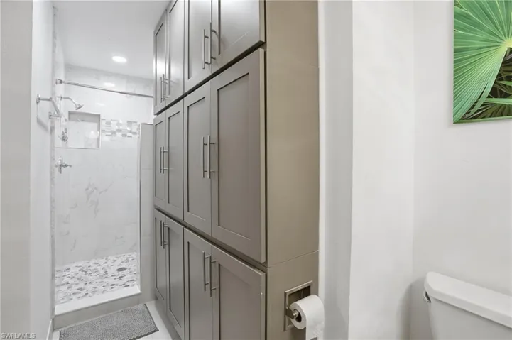Shower stall with marble-look tile walls, a decorative mosaic accent band, and a pebble-finish floor