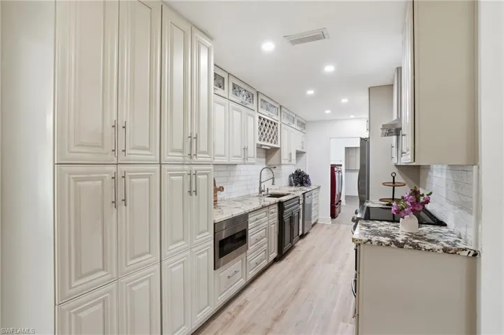 Kitchen featuring extensive light-toned cabinetry, granite-style countertops, stainless steel appliances, and a subway tile backsplash