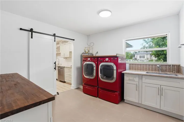 Laundry area featuring barn door entry, a built-in sink with mosaic tile backsplash, white cabinetry, and wood-finish countertop