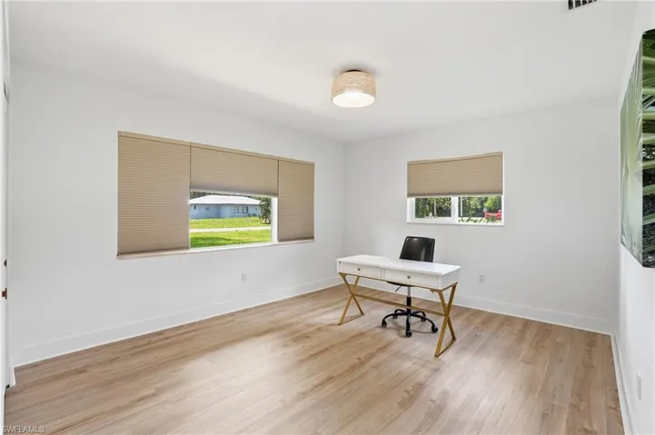 Spacious room with light wood-finish flooring, two large windows with blinds, white baseboards, and a contemporary ceiling light fixture