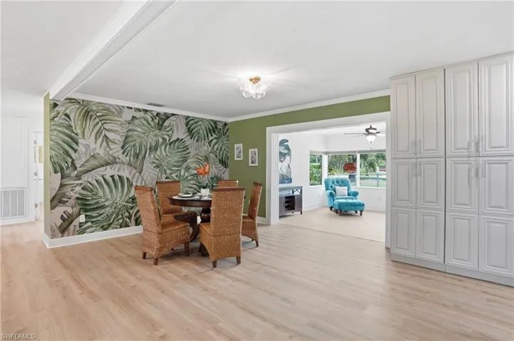 Dining area featuring wood-finish flooring, a decorative accent wall, and a view into an additional living space