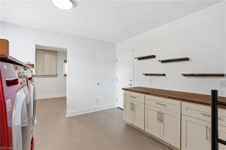 Bright utility room featuring light wood-finish flooring, white cabinetry with wood countertops, and modern floating shelves