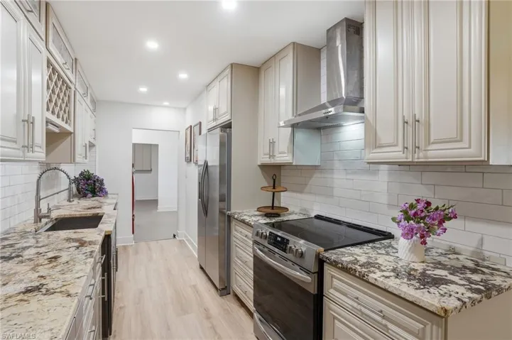 Galley kitchen featuring light-toned cabinetry, granite-style countertops, stainless steel appliances, and a subway tile backsplash