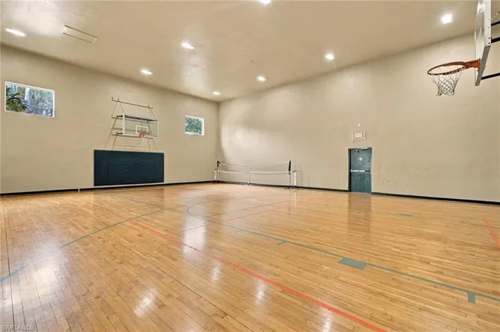 Indoor sports court featuring wood-finish flooring, two basketball hoops, and a volleyball net