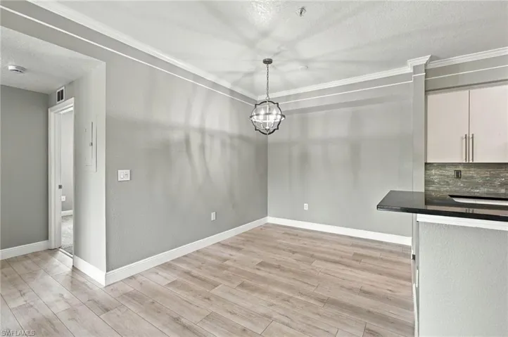 Wood-finish flooring, crown molding, modern chandelier, recessed lighting, and kitchen pass-through with dark countertop