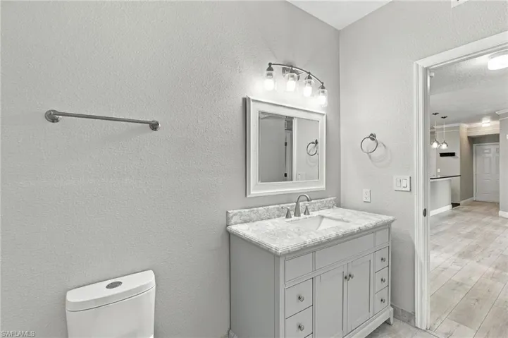 Bathroom featuring a single vanity with stone countertop, undermount sink, brushed nickel faucet, and framed mirror