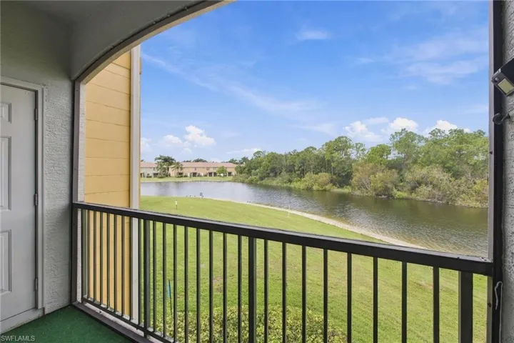 Private balcony with black metal railing, overlooking a body of water, green landscape, and distant buildings