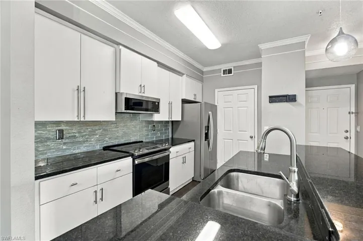 White cabinetry with brushed nickel hardware, dark stone countertops, stainless steel appliances, dual basin sink with gooseneck faucet, and a stone tile backsplash