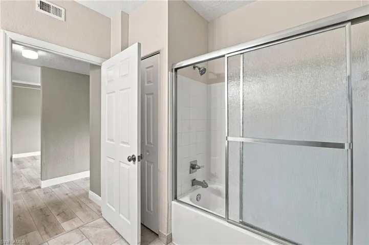 Bathtub with sliding glass enclosure, white subway tile surround, and chrome fixtures