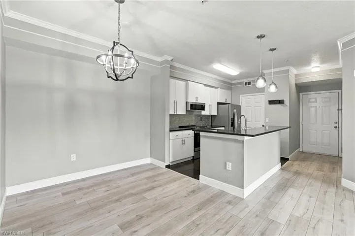 Open-concept living space with light wood-finish flooring, crown molding, and a modern chandelier
