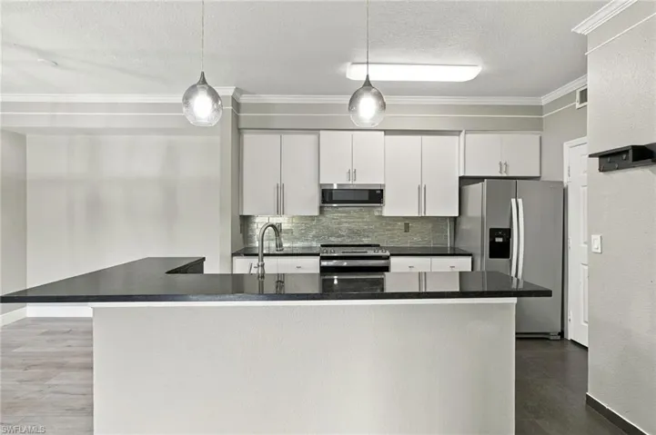 Kitchen featuring stainless steel appliances, dark countertops, white cabinetry, a tile backsplash, and two pendant light fixtures