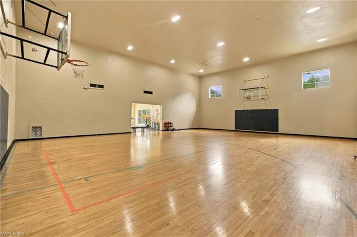 Indoor court with wood-finish flooring, two basketball hoops, and recessed lighting