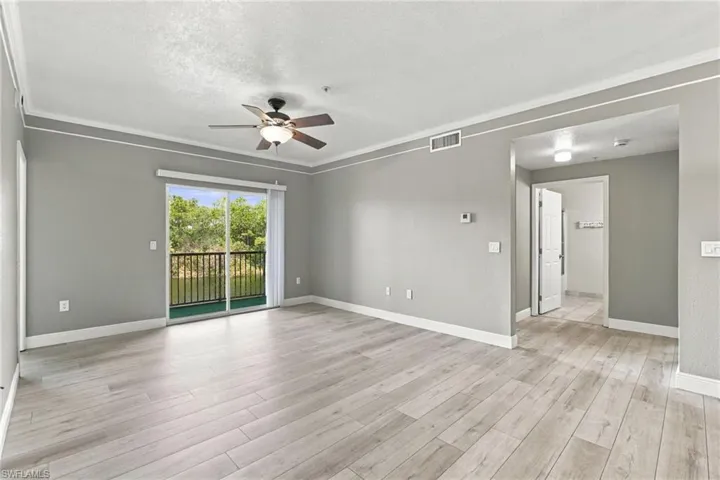 Spacious room featuring light wood-finish flooring, crown molding, and a ceiling fan with integrated lighting