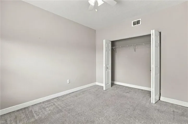 Neutral wall paint, gray carpeting, a built-in closet with bi-fold doors, and a ceiling fan