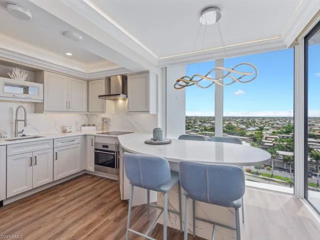Kitchen with expansive windows, wall chimney exhaust hood, light wood-style floors, stainless steel oven, and a breakfast bar
