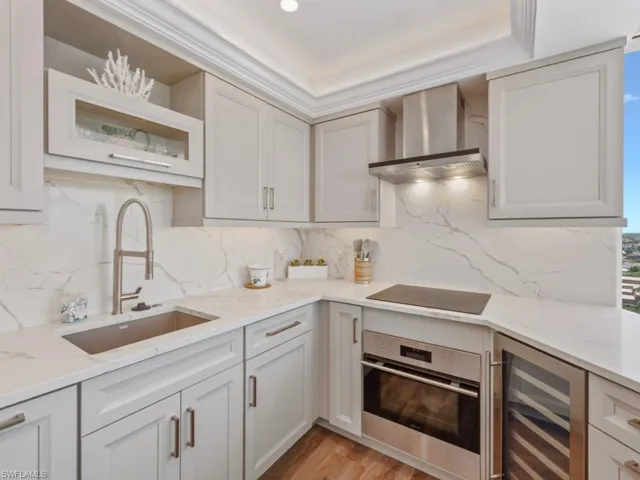 Kitchen with oven, wall chimney exhaust hood, beverage cooler, and light stone countertops