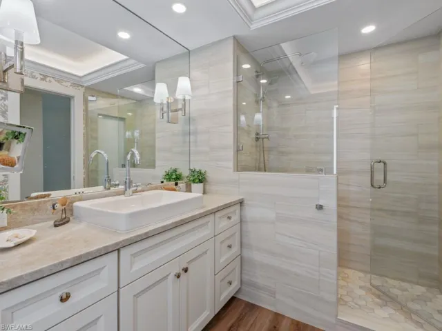 Bathroom featuring a tile shower, vanity, tile walls, ornamental molding, and wood finished floors
