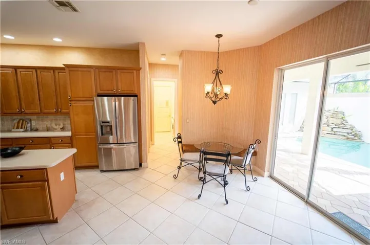 Kitchen with pendant lighting, a notable chandelier, stainless steel refrigerator with ice dispenser, backsplash, and light tile patterned floors