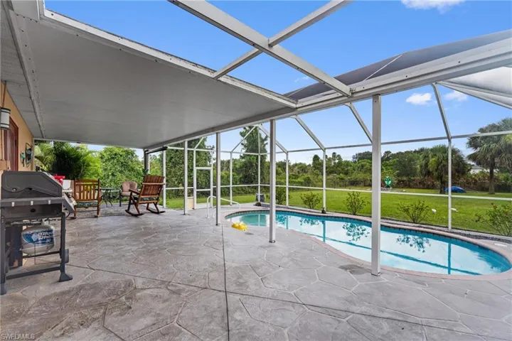 Swimming pool featuring a patio, a grill, a sunroom, a lawn, and glass enclosure