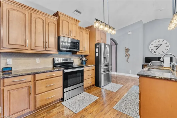 Kitchen with arched walkways, stainless steel appliances, dark stone countertops, vaulted ceiling, and tasteful backsplash