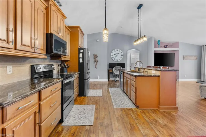 Kitchen with appliances with stainless steel finishes, lofted ceiling, dark stone countertops, pendant lighting, and light wood-style flooring