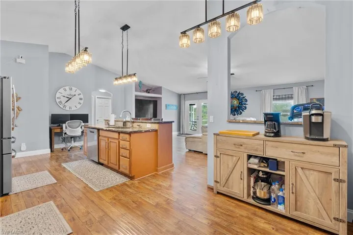 Kitchen featuring a desk, lofted ceiling, light wood finished floors, decorative light fixtures, and dark stone countertops