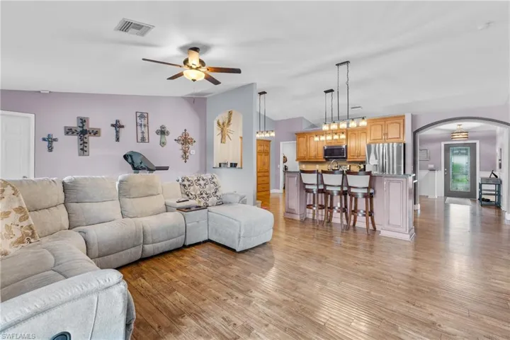 Living area featuring arched walkways, light wood-style flooring, ceiling fan, and lofted ceiling