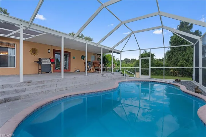 Outdoor pool featuring glass enclosure, a sunroom, area for grilling, and a patio area