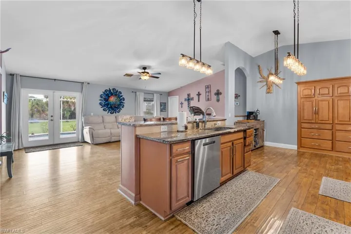 Kitchen featuring open floor plan, brown cabinets, dark stone countertops, light wood-type flooring, and lofted ceiling