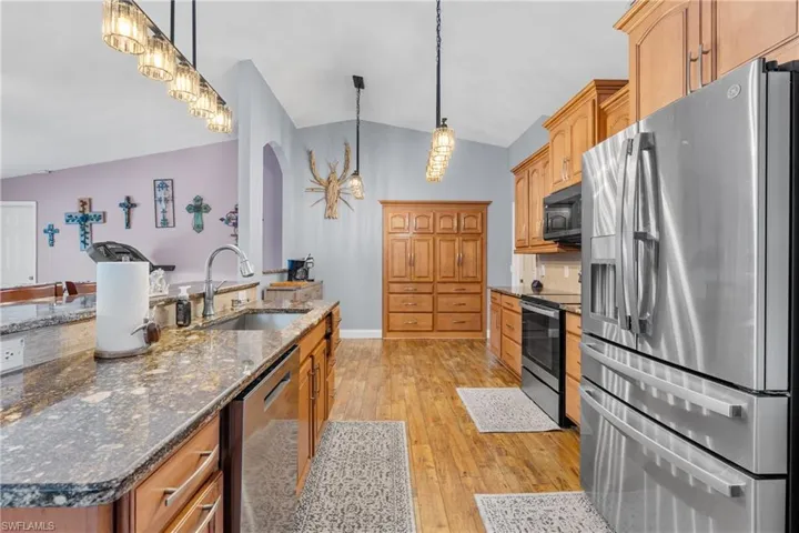 Kitchen featuring stainless steel appliances, lofted ceiling, dark stone counters, light wood finished floors, and decorative light fixtures