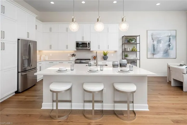 Kitchen with stainless steel appliances, light countertops, a kitchen breakfast bar, white cabinets, and light wood-style flooring