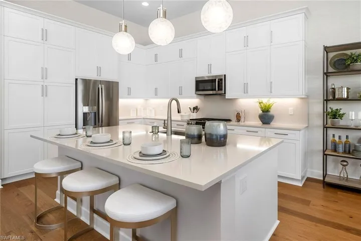 Kitchen featuring appliances with stainless steel finishes, light wood-style floors, white cabinets, a kitchen breakfast bar, and recessed lighting