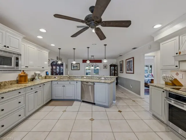 Kitchen featuring stainless steel appliances, light stone counters, gray cabinetry, decorative light fixtures, and ornamental molding