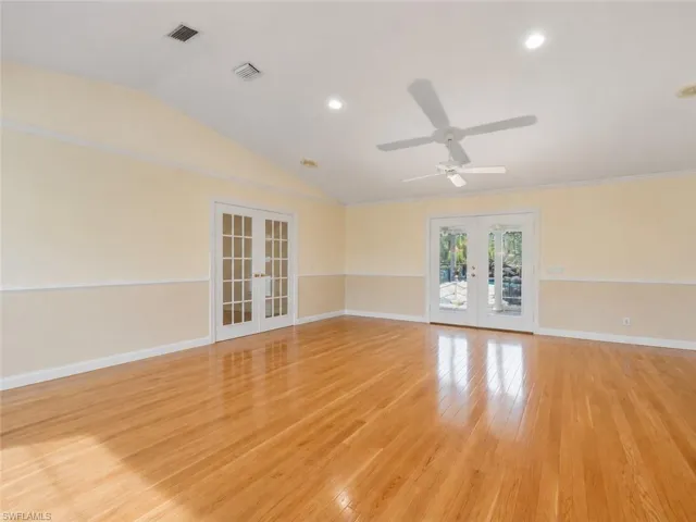 Spacious room featuring wood-finish flooring, a vaulted ceiling, and two sets of French doors