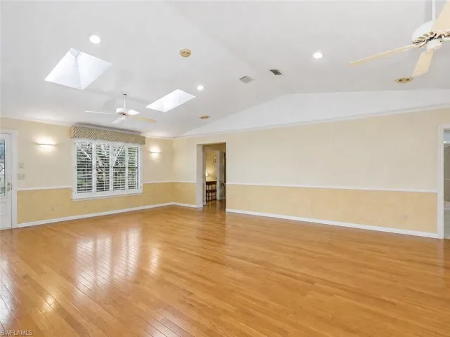 Spacious living area featuring polished wood-finish flooring, vaulted ceilings, and multiple skylights