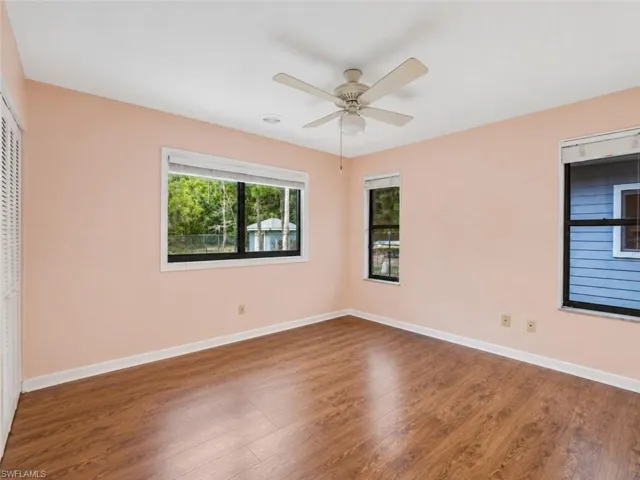 Expansive room featuring wood-finish flooring, light peach walls, and multiple windows