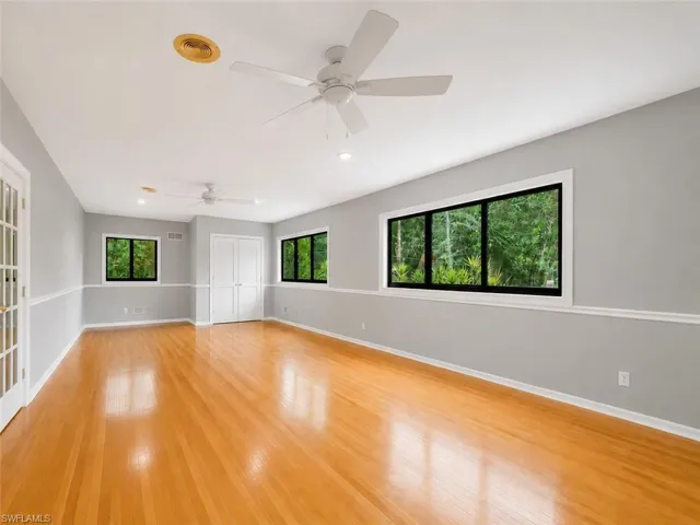 Spacious room featuring wood-finish flooring, light grey walls with white trim, multiple windows with black frames, and dual ceiling fans