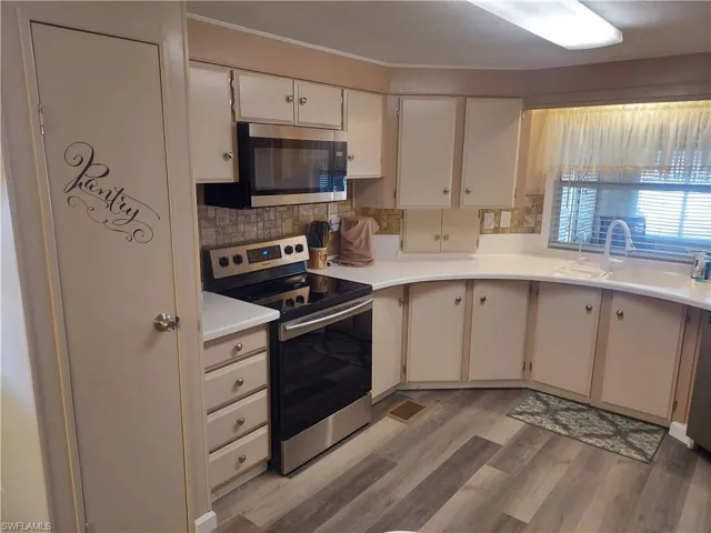 Kitchen with sink, light hardwood / wood-style flooring, white cabinetry, backsplash, and stainless steel appliances