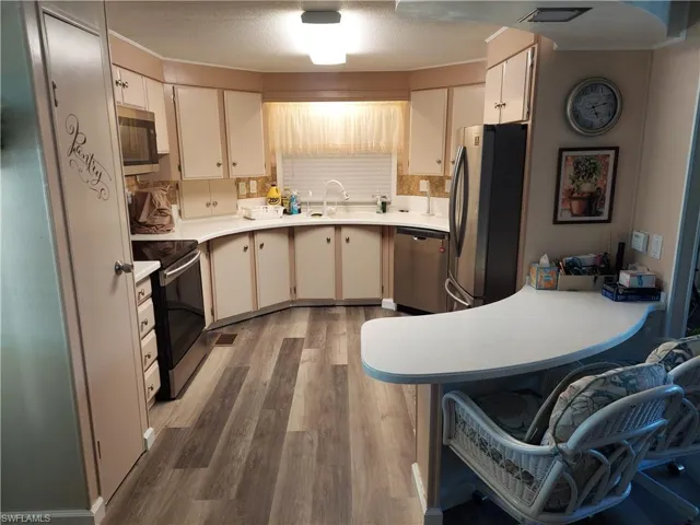 Kitchen with a textured ceiling, stainless steel appliances, sink, white cabinets, and light hardwood / wood-style floors