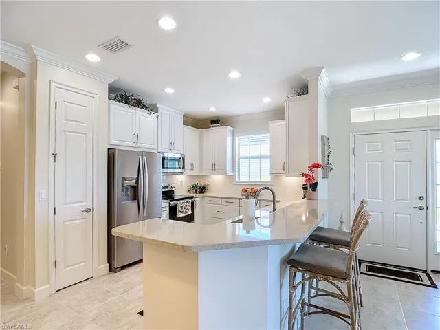 Kitchen with tasteful backsplash, light tile floors, white cabinets, a breakfast bar area can seat four...