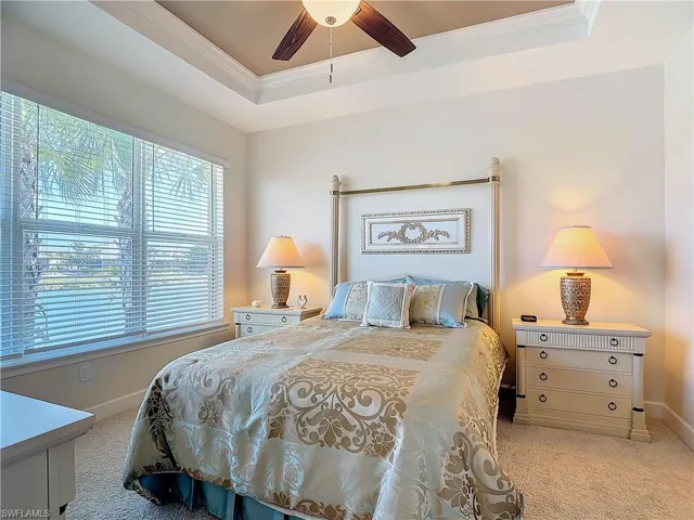 Carpeted bedroom featuring ceiling fan, a tray ceiling, and crown molding