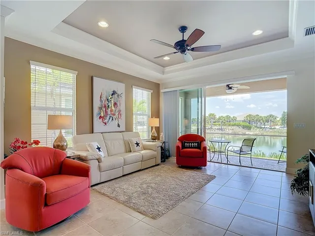 Living room with ceiling fan, a tray ceiling, a wealth of natural light, and a water view