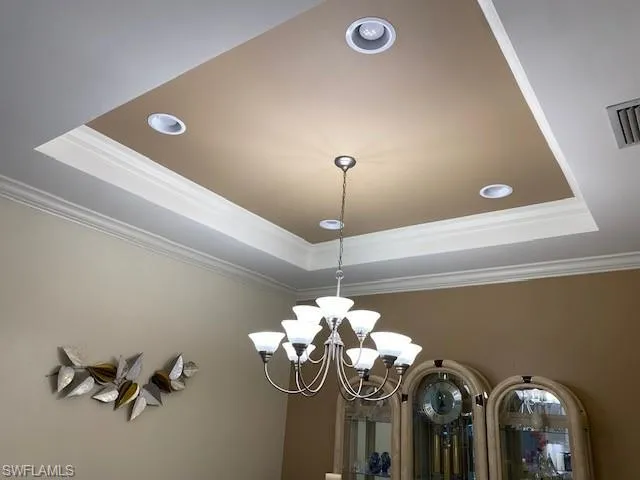 Interior details featuring a tray ceiling, ornamental molding, and a notable chandelier
