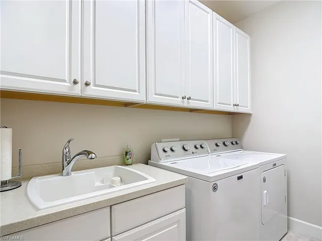 Laundry washing area with sink, washing machine and clothes dryer, with plenty cabinets for extra storage.