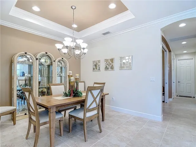 Tiled dining room with a tray ceiling, crown molding, and an inviting chandelier