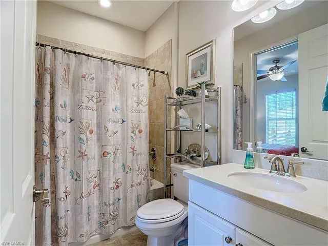 Full guest bathroom with oversized vanity, toilet, ceiling fan, and shower / tub combo with curtain
